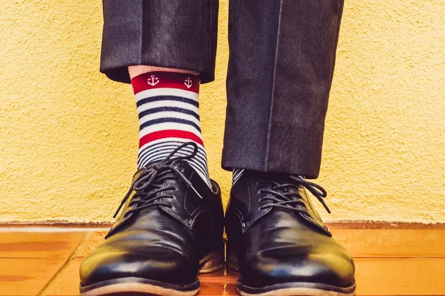 Un homme porte des chaussettes fantaisie rayées rouge, blanc, bleu avec un motif d'ancre et des chaussures noires.