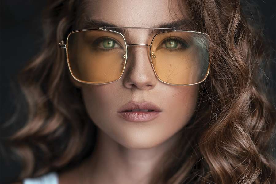 Gros plan d'une femme portant des lunettes aux verres teintés et un maquillage et lunettes soigné qui met en valeur ses yeux verts.