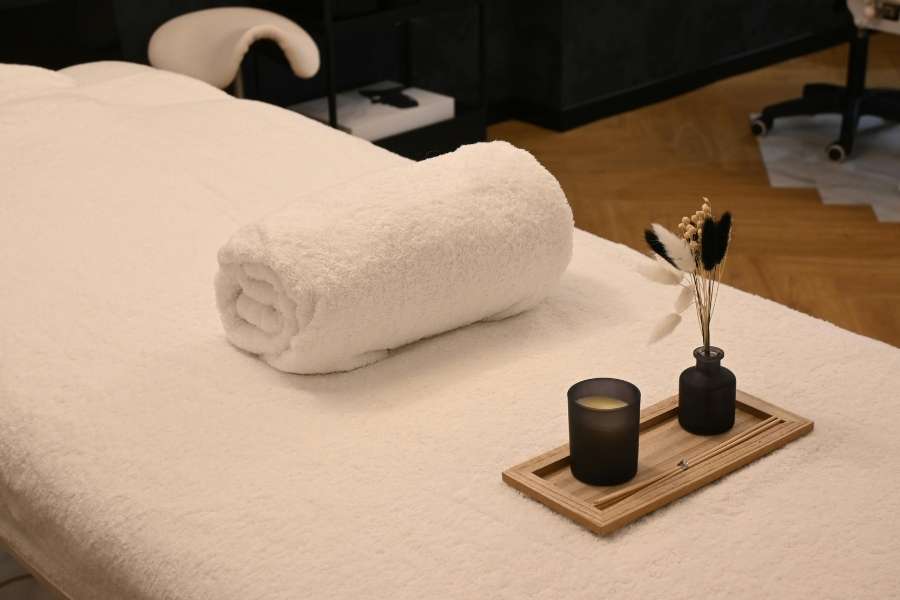 Table de massage recouverte d'un drap blanc propre avec une serviette enroulée et un plateau de bougies dans un spa de luxe.