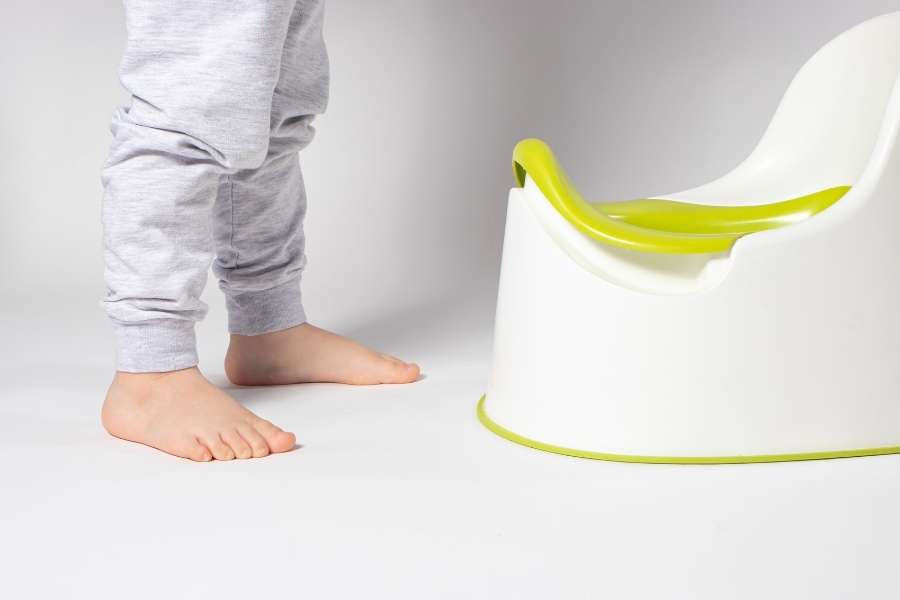 Pieds nus d'un enfant face à un pot vert et blanc sur fond neutre pour l'apprentissage du pot.